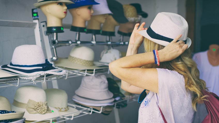 A woman trying a hat on the street.