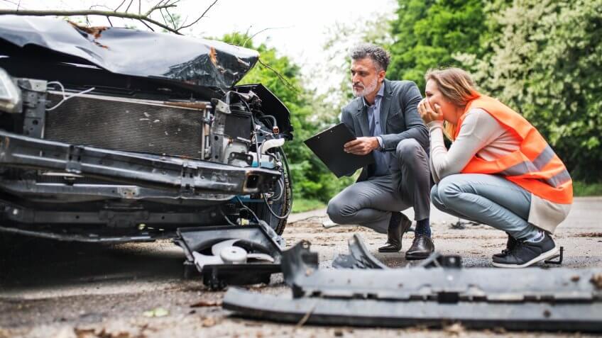 An insurance agent and a woman driver looking at the car on the road after an accident.