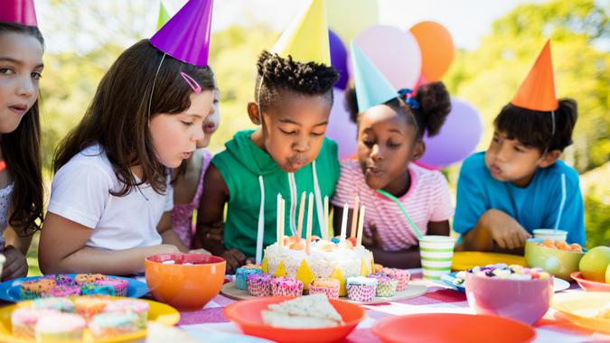 Cute children blowing together on the candle during a birthday party on a park.