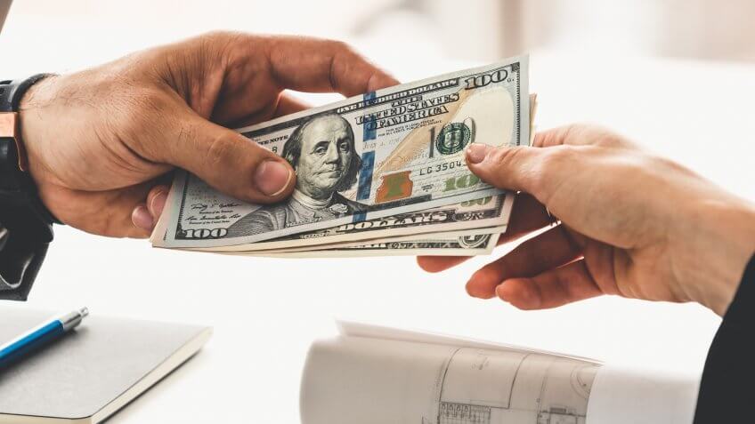 Businessman hand sending money to another business person.