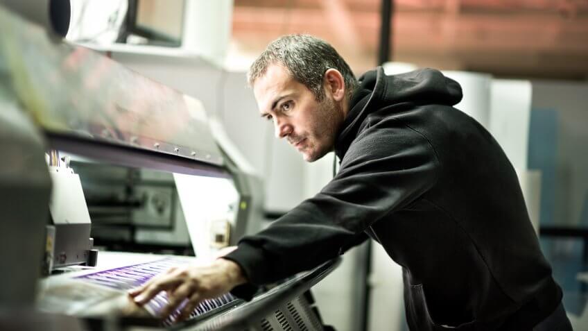 Skilled worker operating on industrial printer inside the printing factory.