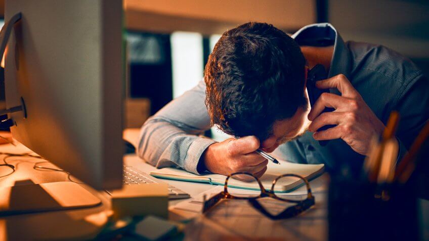 Shot of a young businessman looking stressed out while talking on a cellphone in an office.