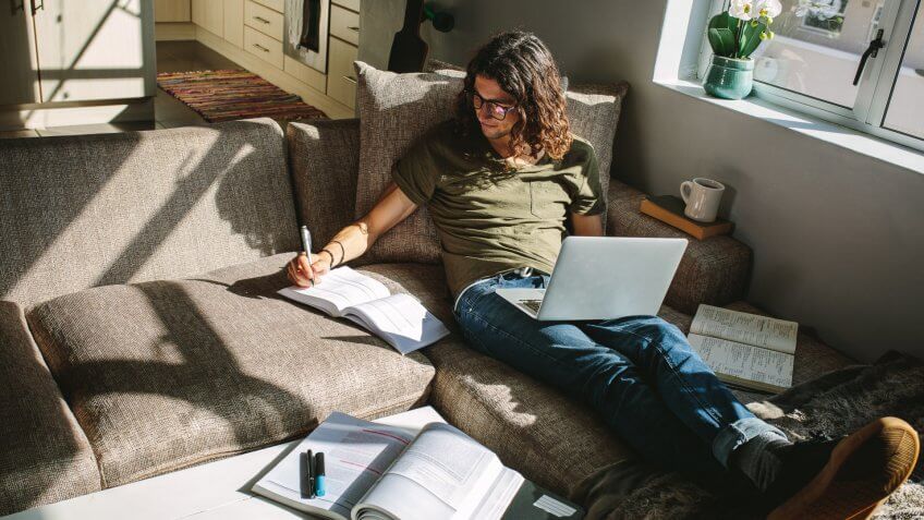 Student studying for exams sitting at home comfortably on a couch.
