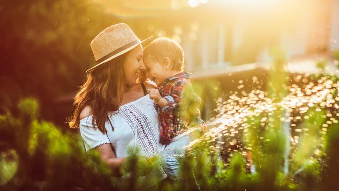 Family in the garden in sunset Mother and her little sun watering plants in garden in summer.