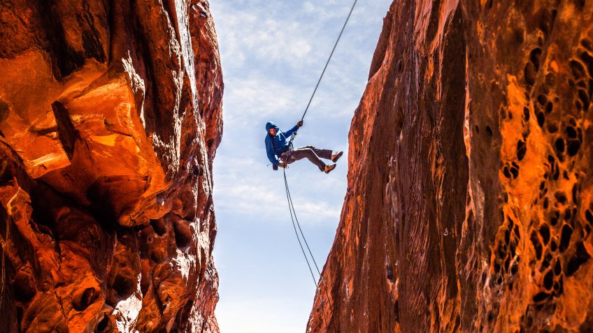 A rock climber kicks off the wall while descending into a slot canyon in Red Rock National Recreation Area.