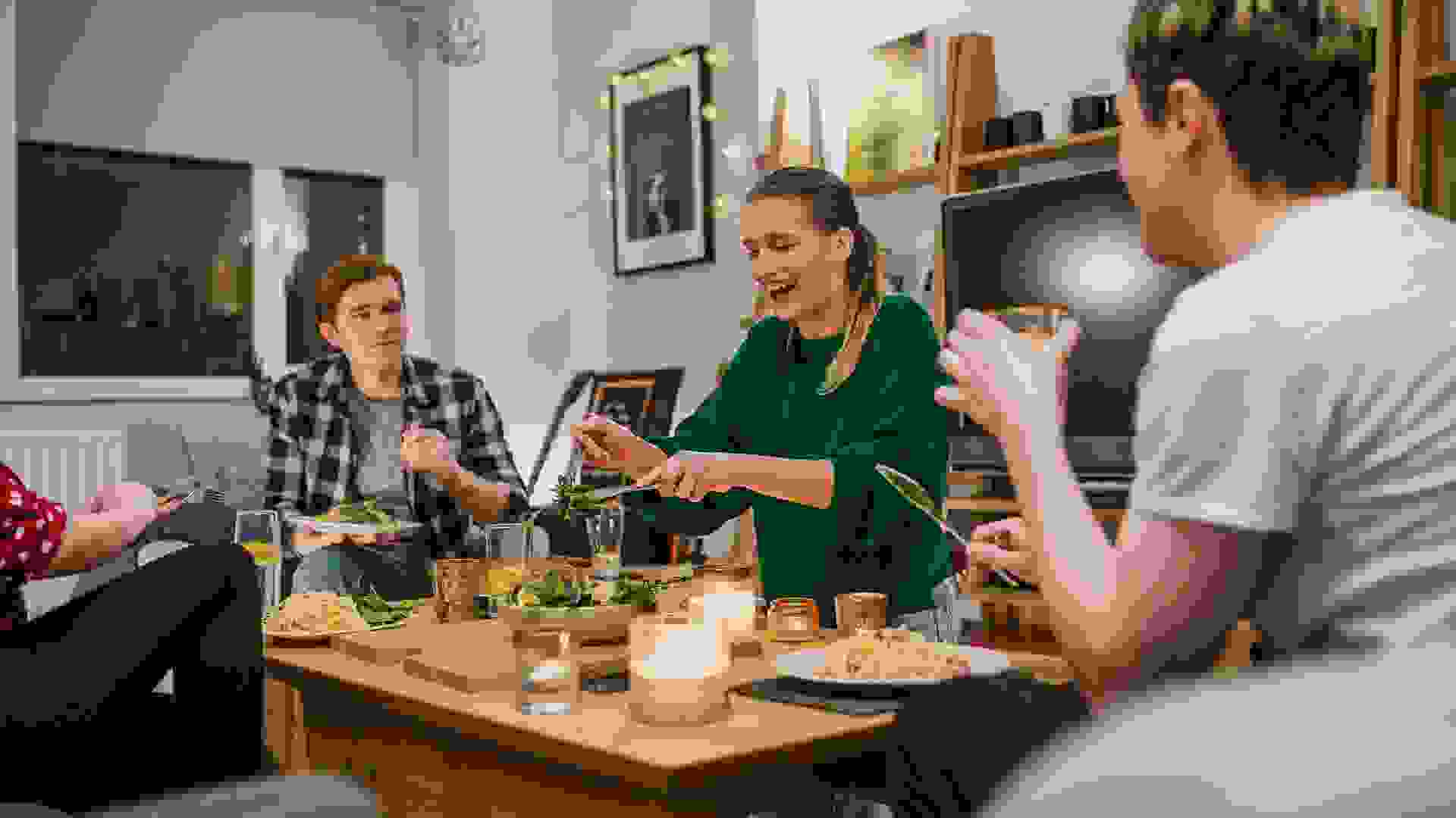 Two young couples are having a dinner party and one woman is laughing while serving salad.