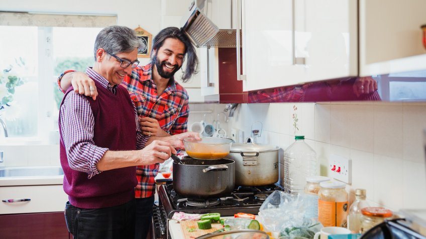 Mid adult man is looking over his father's shoulder as he prepares a curry at home.