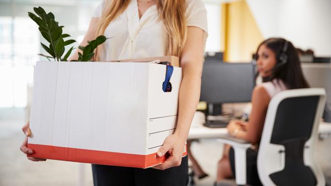Fired female employee holding box of belongings in an office.