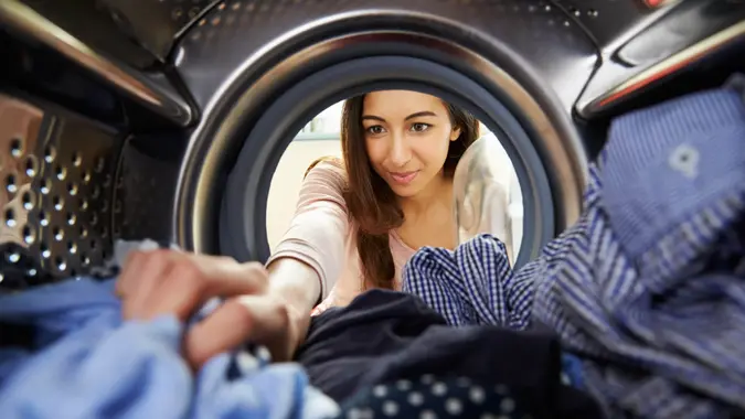 Woman Doing Laundry Reaching Inside Washing Machine.