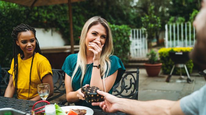 Woman covering mouth while receiving gift by man Happy young woman covering mouth while receiving gift by man.
