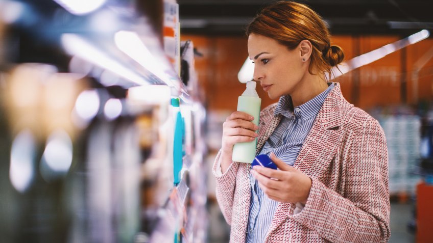 Attractive smiling brunette holding and smelling a bottle of shampoo at supermarket.