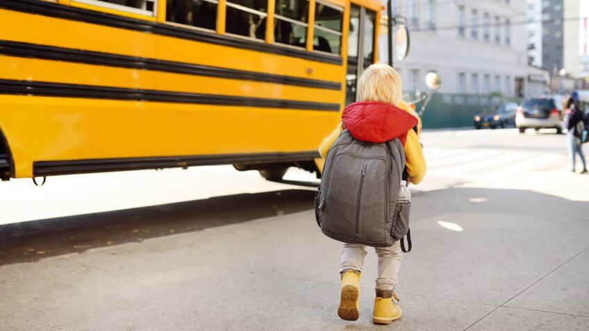 Pupil with schoolbag with yellow school bus on background.
