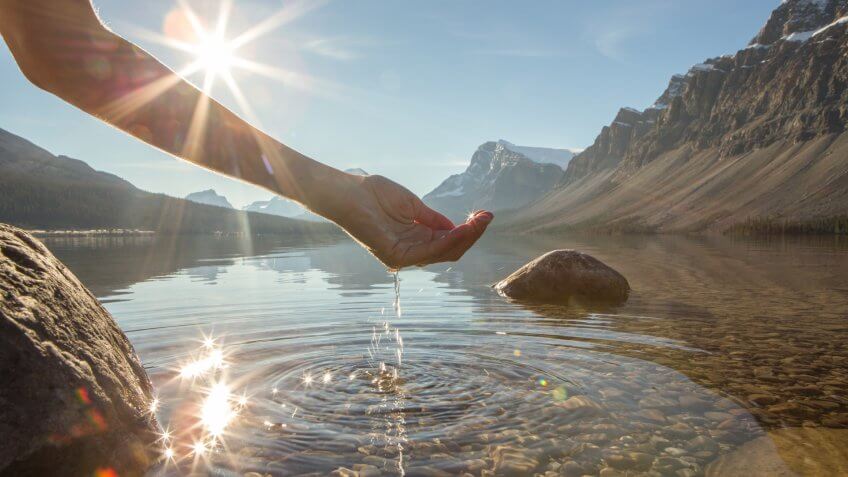 Human hand cupped to catch the fresh water from the lake, sunlight from sunset passing through the transparence of the water.
