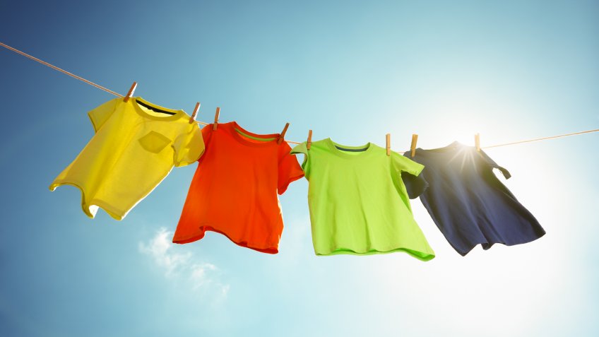 T-shirts hanging on a clothesline in front of blue sky and sun.