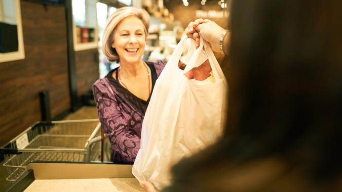 Shot of a mature woman taking a shopping bag from the cashier at a supermarket.