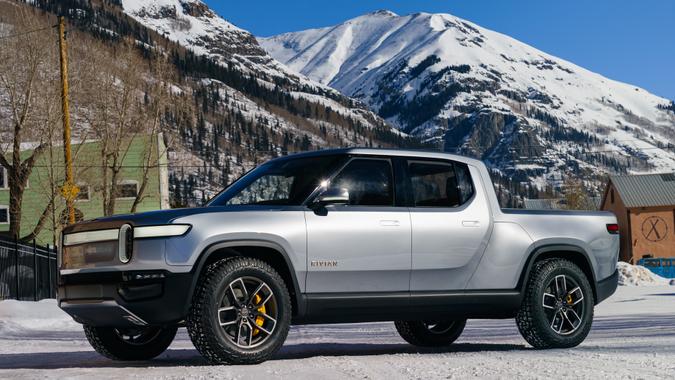 Rivian R1T with snow-capped mountain and blue sky in background.