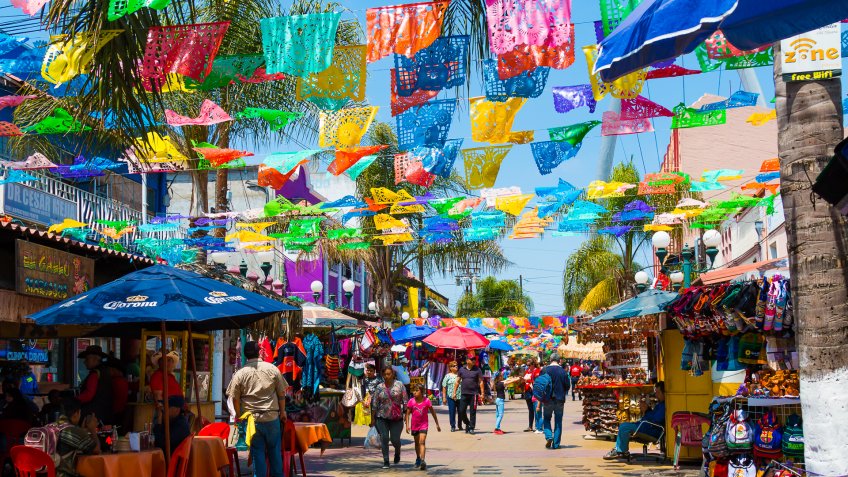 Tijuana, Baja California/Mexico - June 20, 2018: People shop and walk below colorful hanging flags at Plaza Santa Cecilia, a historic Mexican square in the heart of the city.