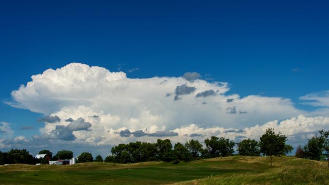 Gathering storm clouds over a tree line and distant farm buildings, Ankeny, Iowa - Image.