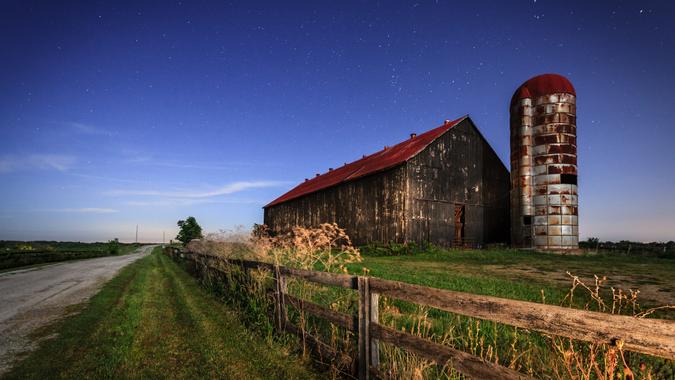 Scenic nighttime image of an old farm barn and a country road in moonlight.