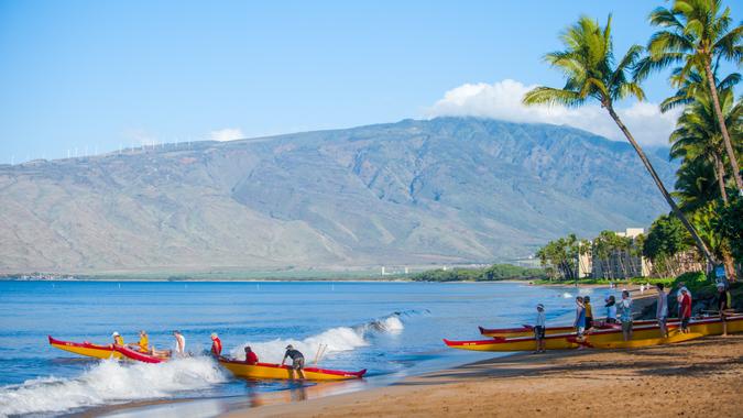 Maui, Hawaii, USA - March 15, 2012: People paddle outrigger canoes off the beach at sunrise.