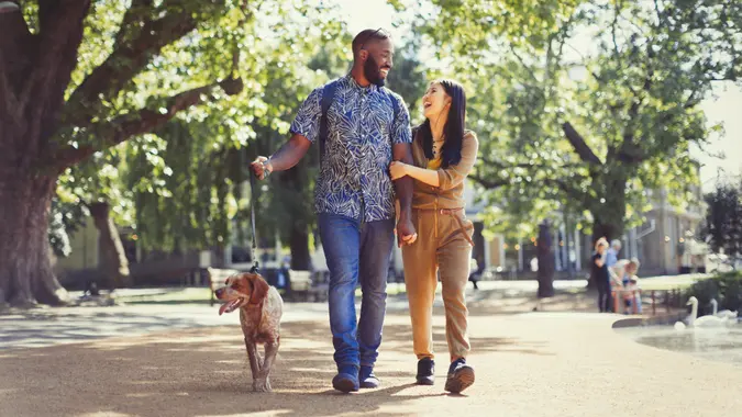 Happy young couple walking dog in sunny park.