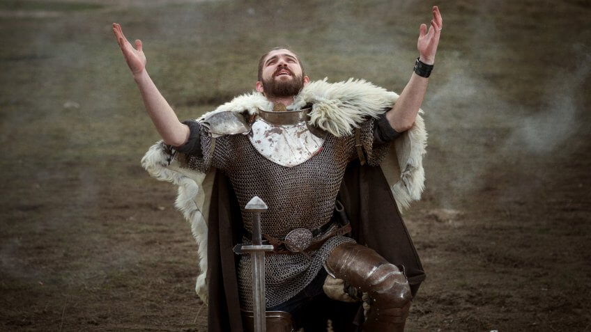 Knight in armor knelt down and pray raised his head to heaven.