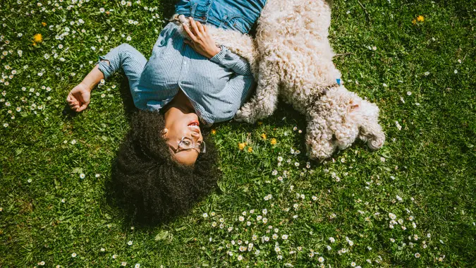A happy young adult woman enjoys time at a park with her standard poodle, running, playing, and relaxing with the dog.
