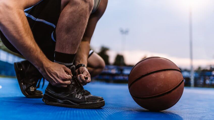 Photo of Unrecognizable Person, Basketball male Caucasian young player tying sport shoes in the summer evening with a basketball by his side.