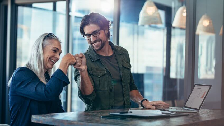Young businessman and senior businesswoman making a fist bump at office.
