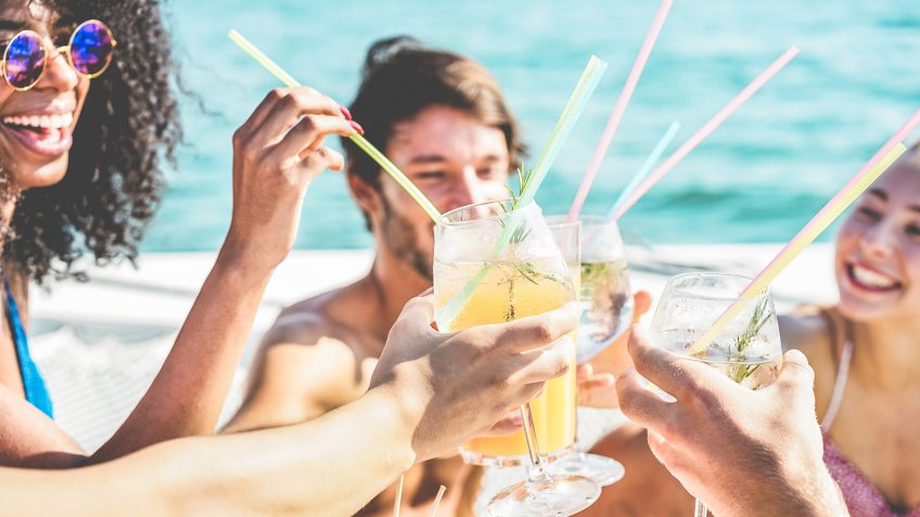 Happy friends drinking and cheering with tropical cocktails at boat party - Young people having fun in sea excursion - Youth lifestyle, vacations and summer concept - Focus on close up glasses.
