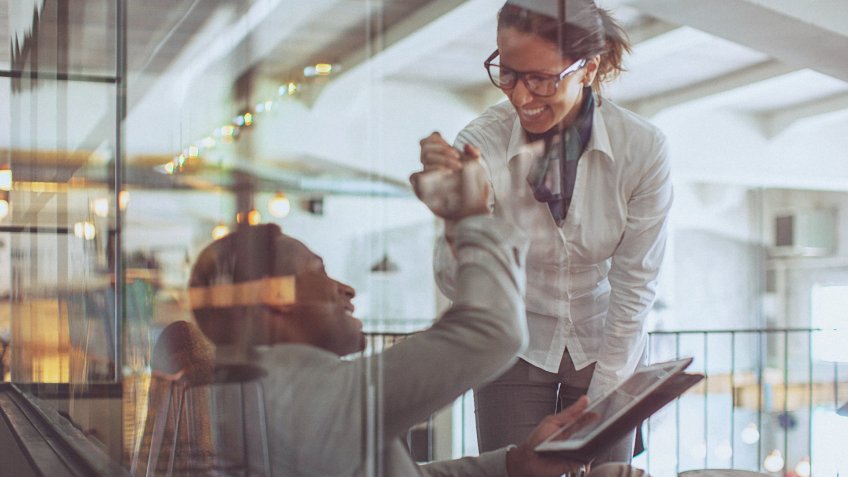 Young businessman and businesswoman giving each other a high five in a modern office space.