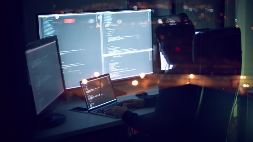 Computer programmer writing code in front of the monitors at late night.