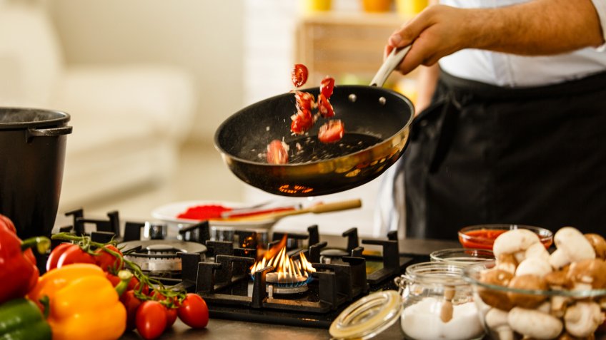 Chef tossing vegetables from cooking pan, preparing healthy meal.