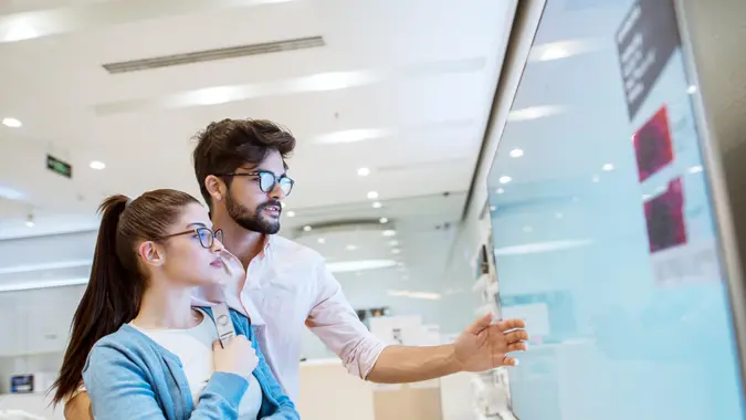 Joyful young attractive multiracial couple checking out plasma TVs in the electronic store.