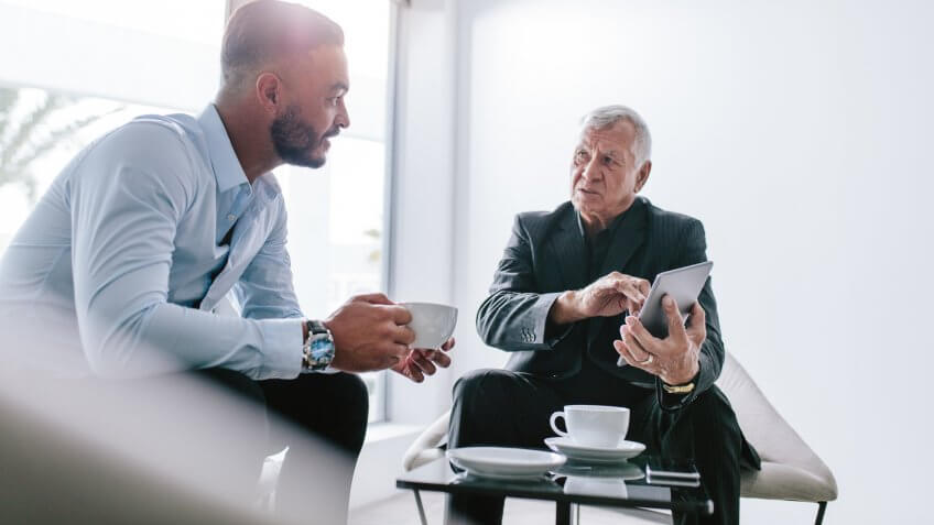 Two businessman sitting in office lobby discussing work over a cup of coffee.