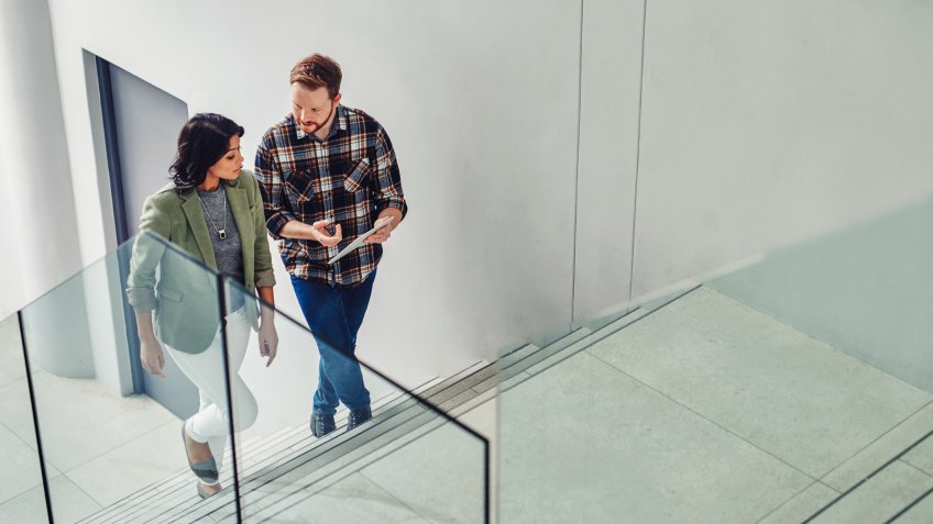 Shot of two young coworkers using a digital tablet while walking up stairs in a modern office.