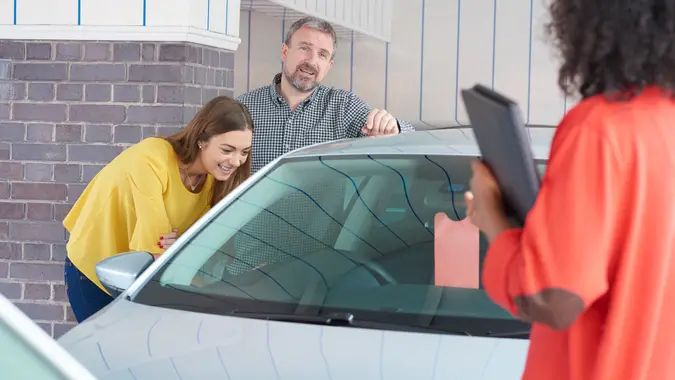 A mature man and his young daughter are looking at cars in a car showrooms .