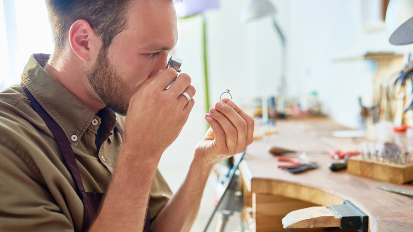 Side view portrait of jeweler inspecting ring through magnifying glass in workshop.