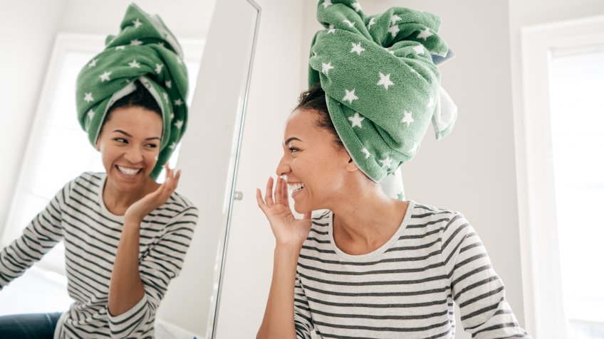 Woman with towel smiling to mirror.