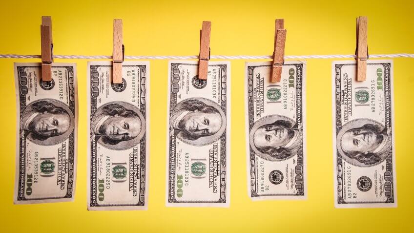 500 dollars hanging on a clothesline against a yellow background.