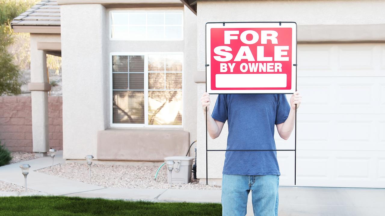 "Photo of a man standing in front of his house, hiding behind a For Sale sign.
