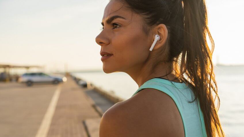 Tired fitness woman sweating taking a break listening to music on phone after difficult training.