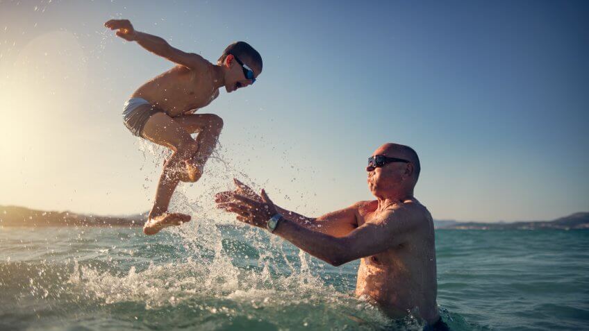 Little boy playing with his grandfather in the sea.