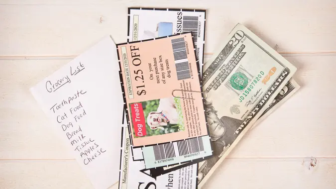 a grocery list with coupons and cash on a table top.