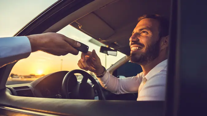Happy businessman taking the car keys from unrecognizable person at sunset.
