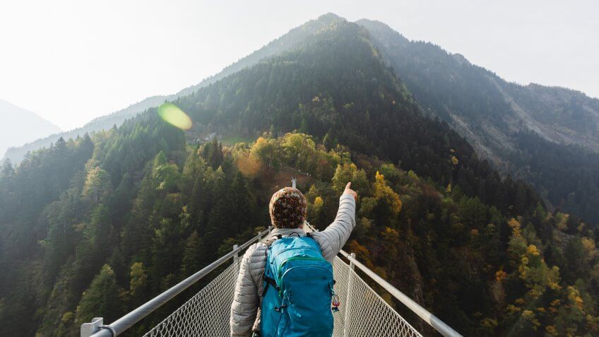 Solo hiker on suspension bridge between two mountain valleys.