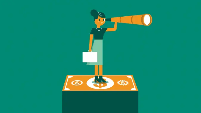 Businesswoman holding telescope standing on currency looking into distance.