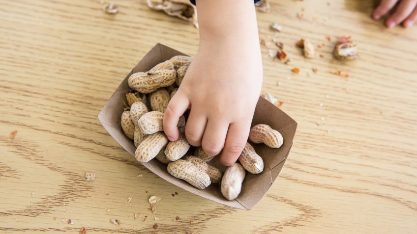 Unrecognizable little boy sits at a table eating peanuts.