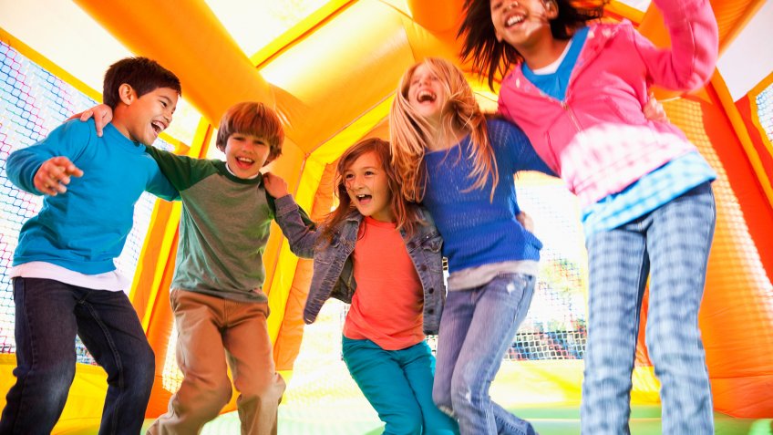 Multi-ethnic group of excited children (ages 7 to 10 years) jumping in inflatable bouncy castle.