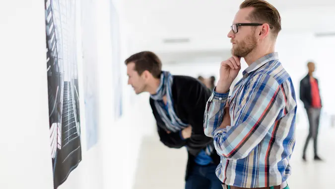 Two multi ethnic visitors of an art gallery looking at artwork hanging on the wall.
